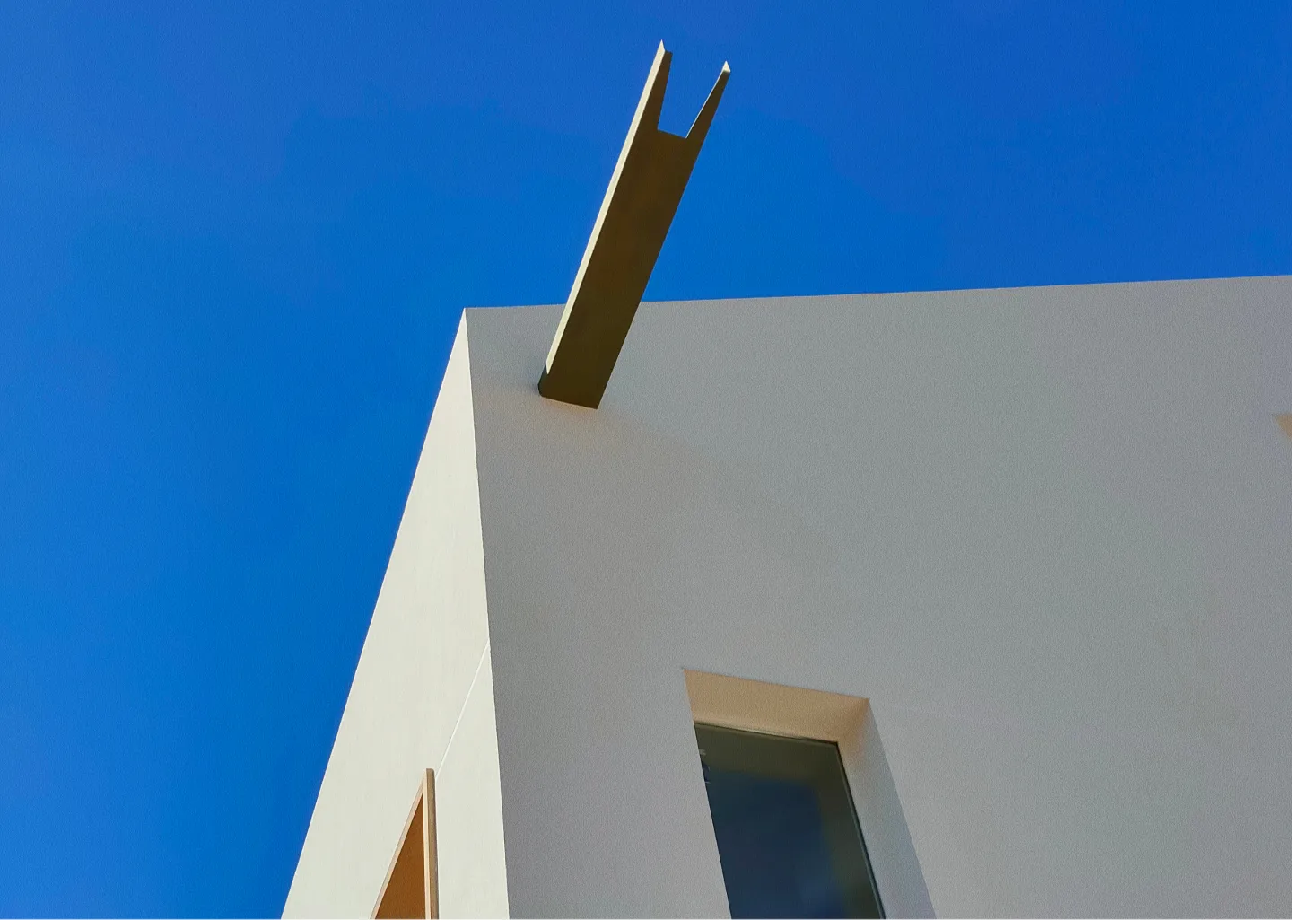 Vista en ángulo del edificio blanco de líneas minimalistas contra un cielo azul claro. Un caño de estilo moderno y sobrio sobresale del borde del tejado, creando un contraste arquitectónico moderno.
