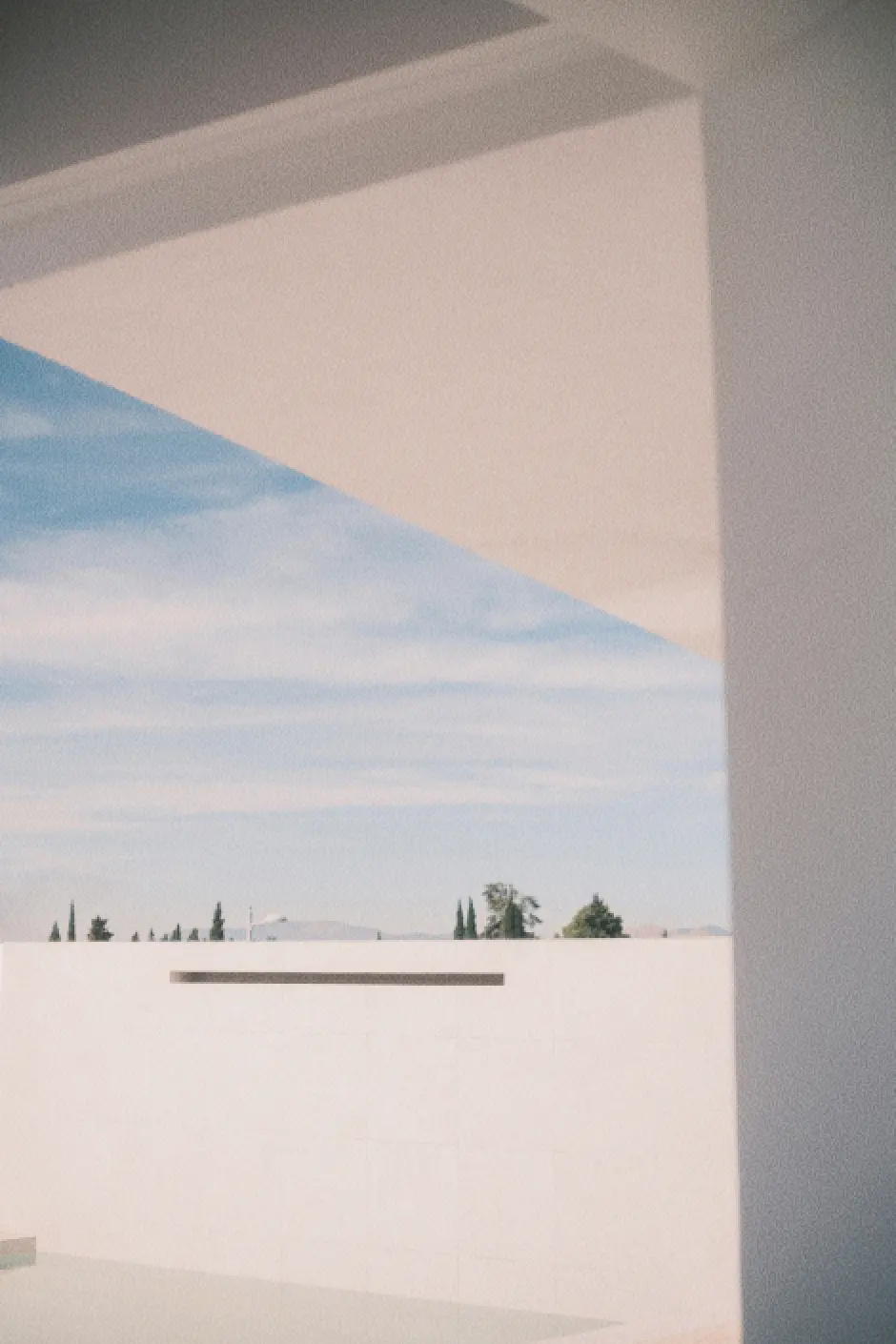 Escena arquitectónica moderna de la piscina de la vivienda, con una pared blanca, sombras geométricas y Sierra Nevada al fondo bajo un cielo despejado. Los árboles dispersos en la distancia crean un ambiente minimalista y sereno.