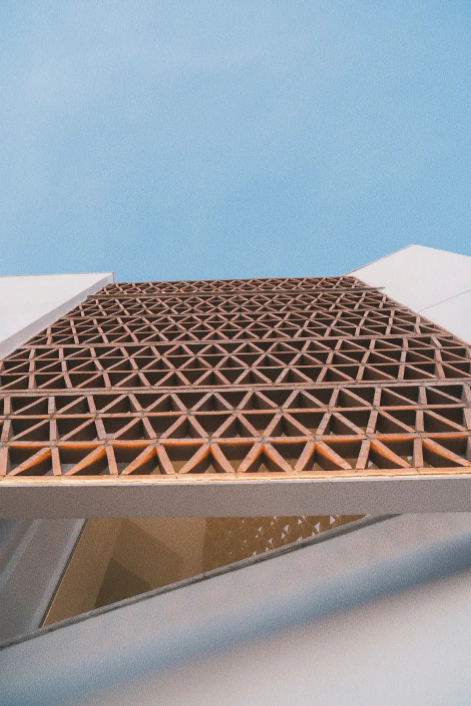 Detalle arquitectónico geométrico de una fachada con una celosía de ladrillo sobre un cielo azul claro, que transmite una sensación de modernidad y amplitud.