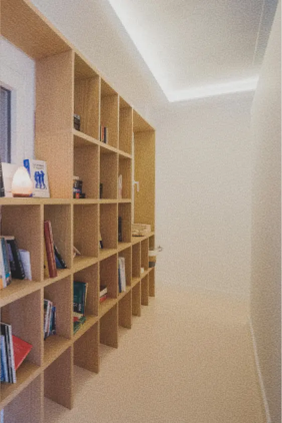 Un pasillo bien iluminado con estanterías de madera repletas de libros de todo tipo y una lámpara que desprende una luz cálida, creando un ambiente acogedor y agradable.