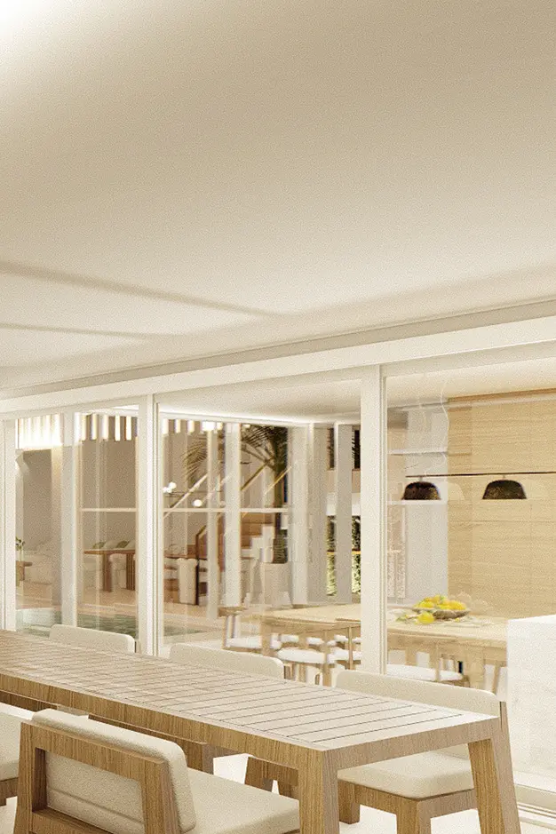 Comedor con una larga mesa de madera y sillas acolchadas. Las puertas acristaladas dejan entrever un amplio espacio interior, decorado con plantas, y un ambiente cálido y acogedor.