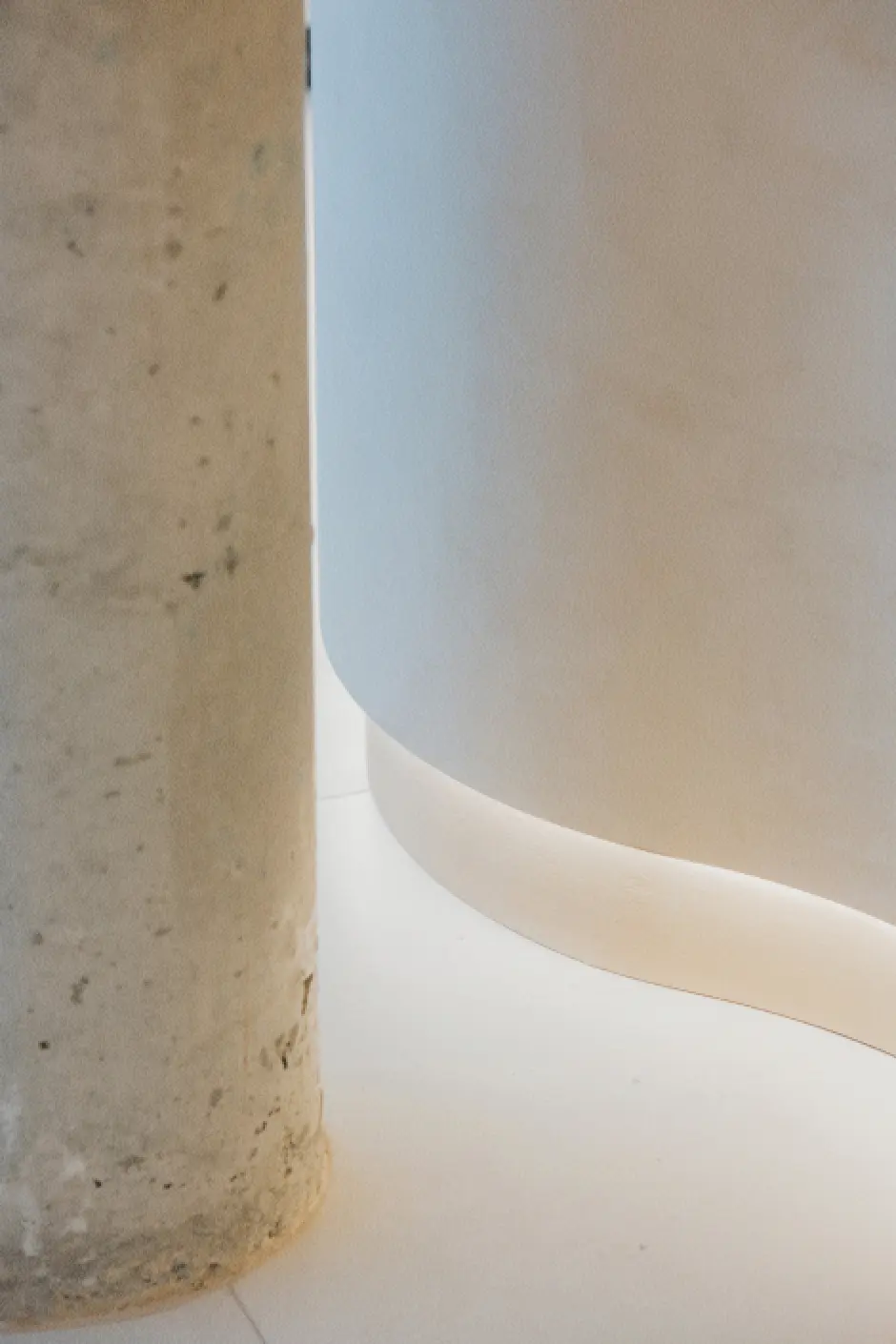 Detalle de la zona inferior del mostrador blanco con la luz LED que ilumina sutilmente el bajo del mismo. Se aprecia junto a él la base de una columna de hormigón visto.